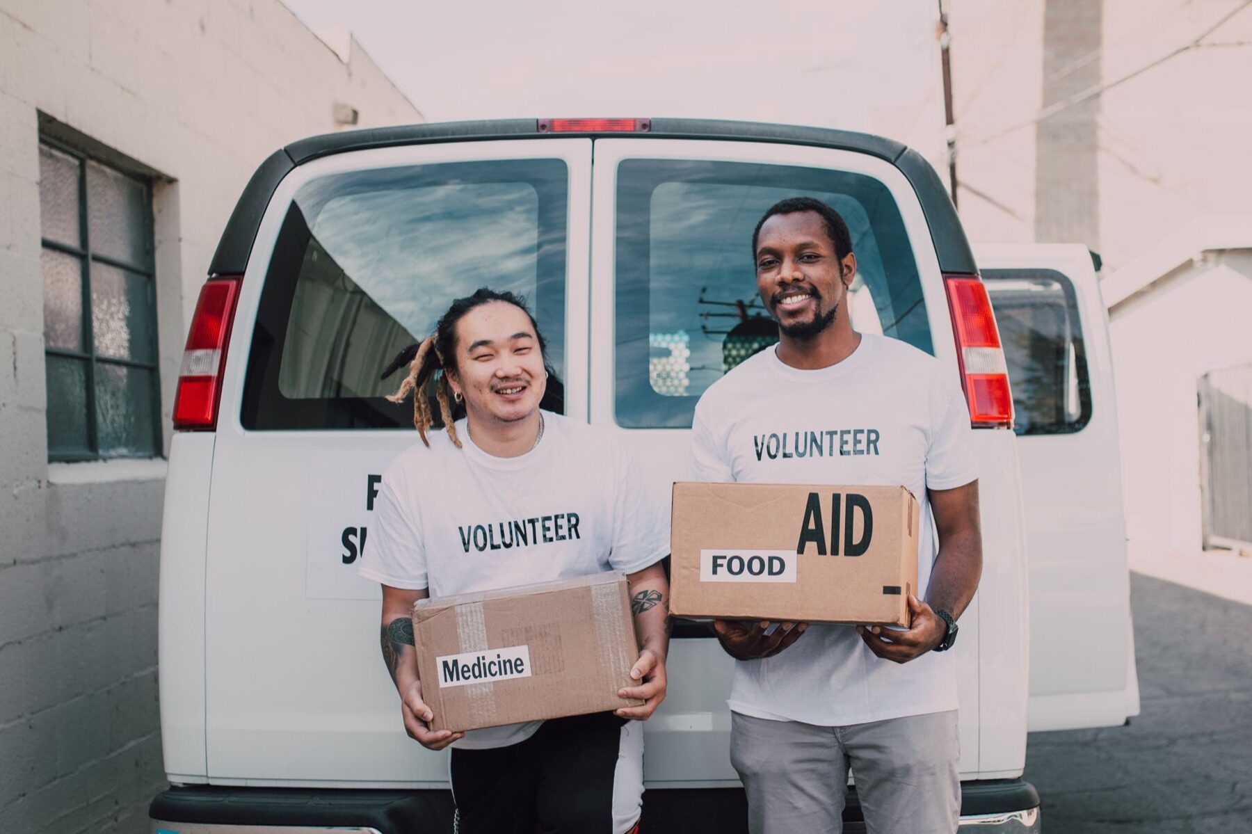Two smiling volunteers carrying a Food Aid box at the back of a white food supplies van